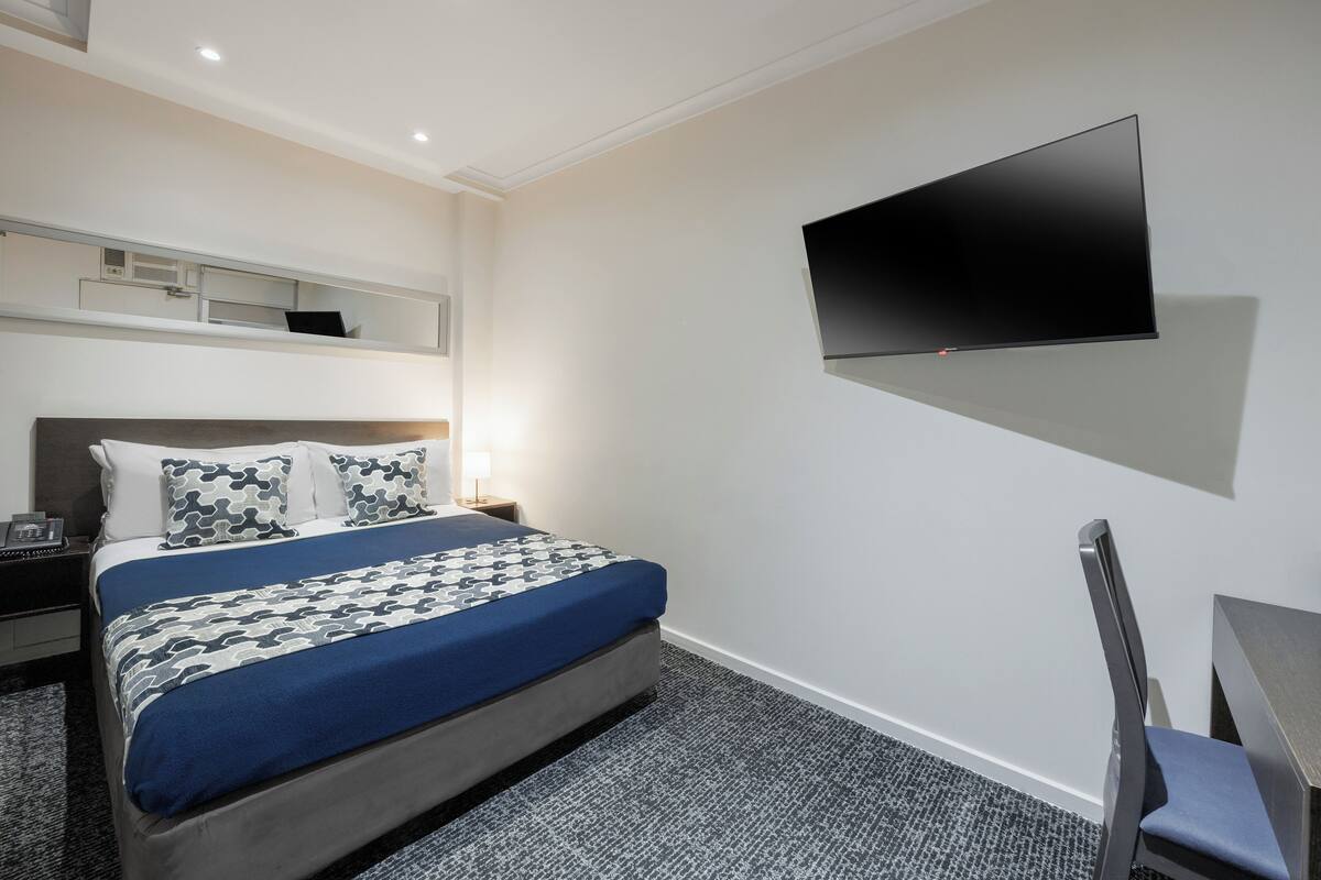 Habitación de hotel con cama, escritorio, silla, televisor de pantalla plana montado en la pared y una mesita.