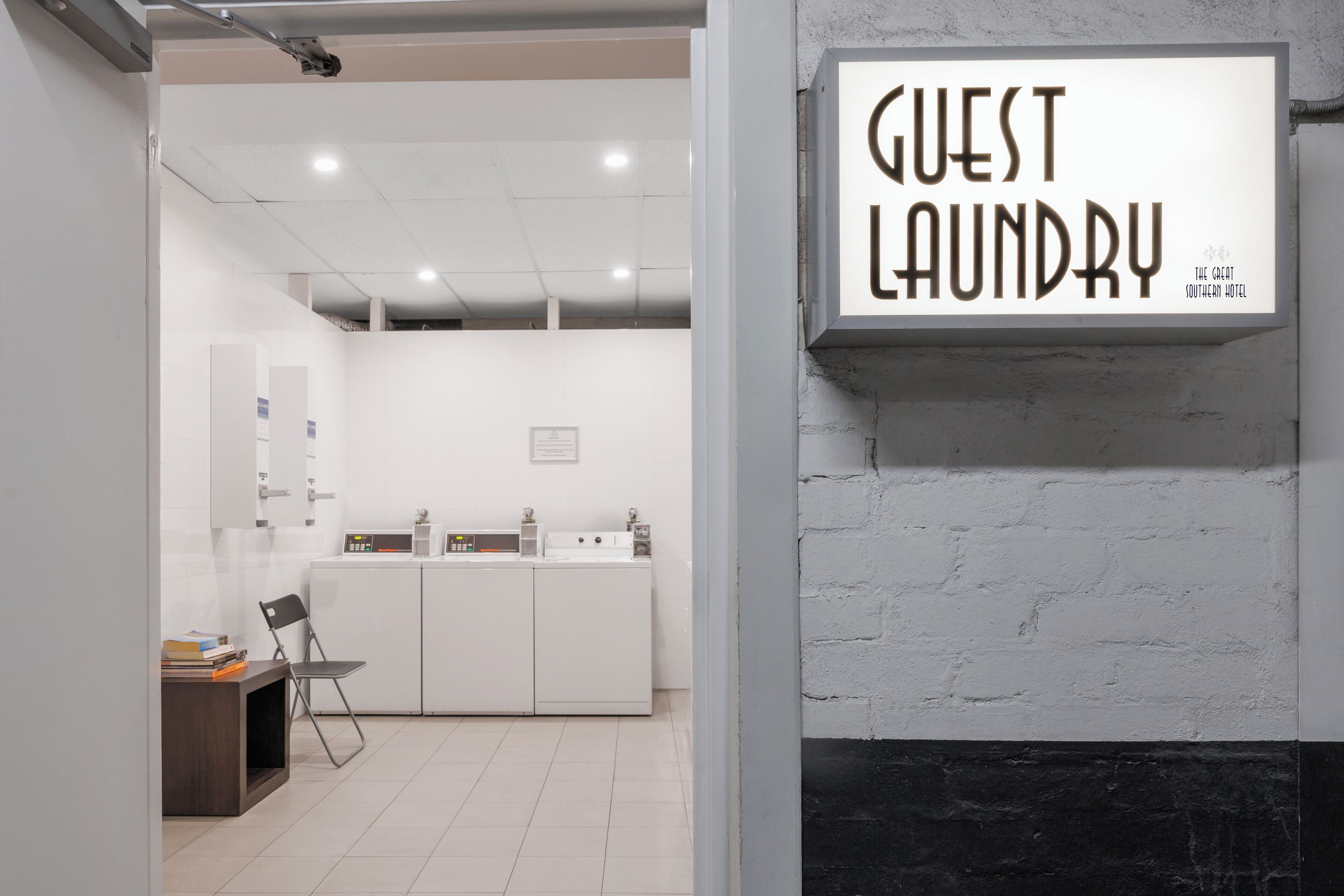 Habitación de hotel con un letrero que dice 'Guest Laundry', un escritorio con una silla y vistas al baño.