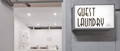 Habitación de hotel con un letrero que dice 'Guest Laundry', un escritorio con una silla y vistas al baño.