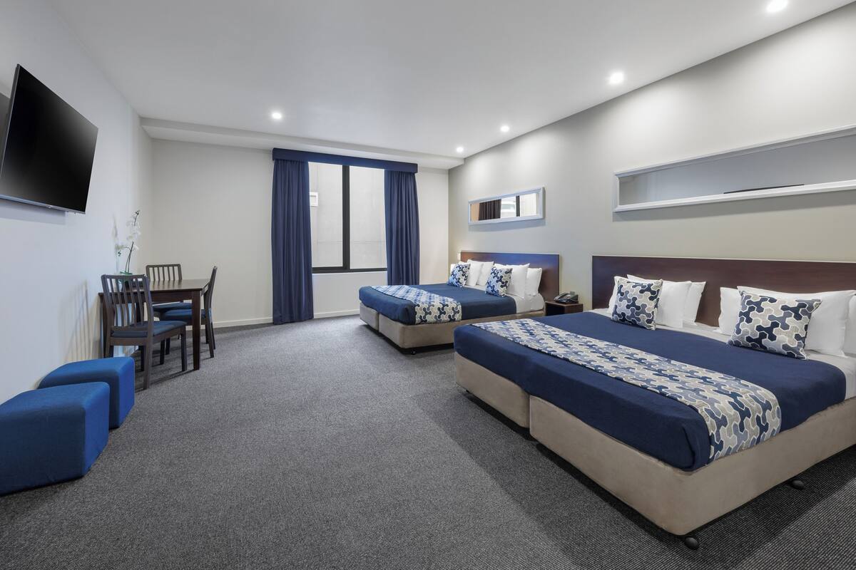 Habitación de hotel con dos camas, un escritorio y una televisión.