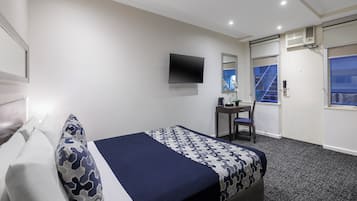 A hotel room with a bed, a desk, a chair, a TV, and a window with a view of a staircase.