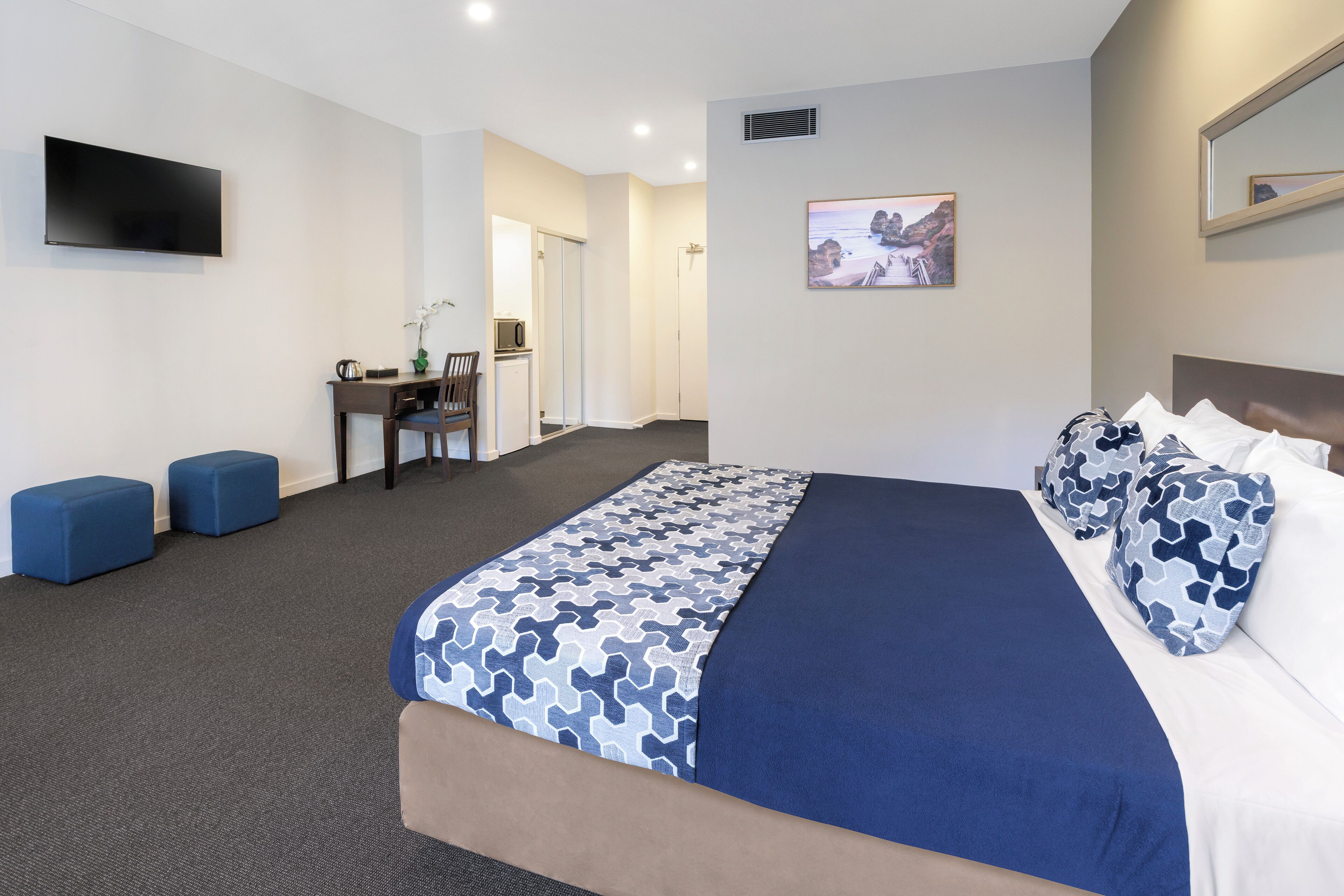 A hotel room with a bed, a desk, a chair, and a TV.