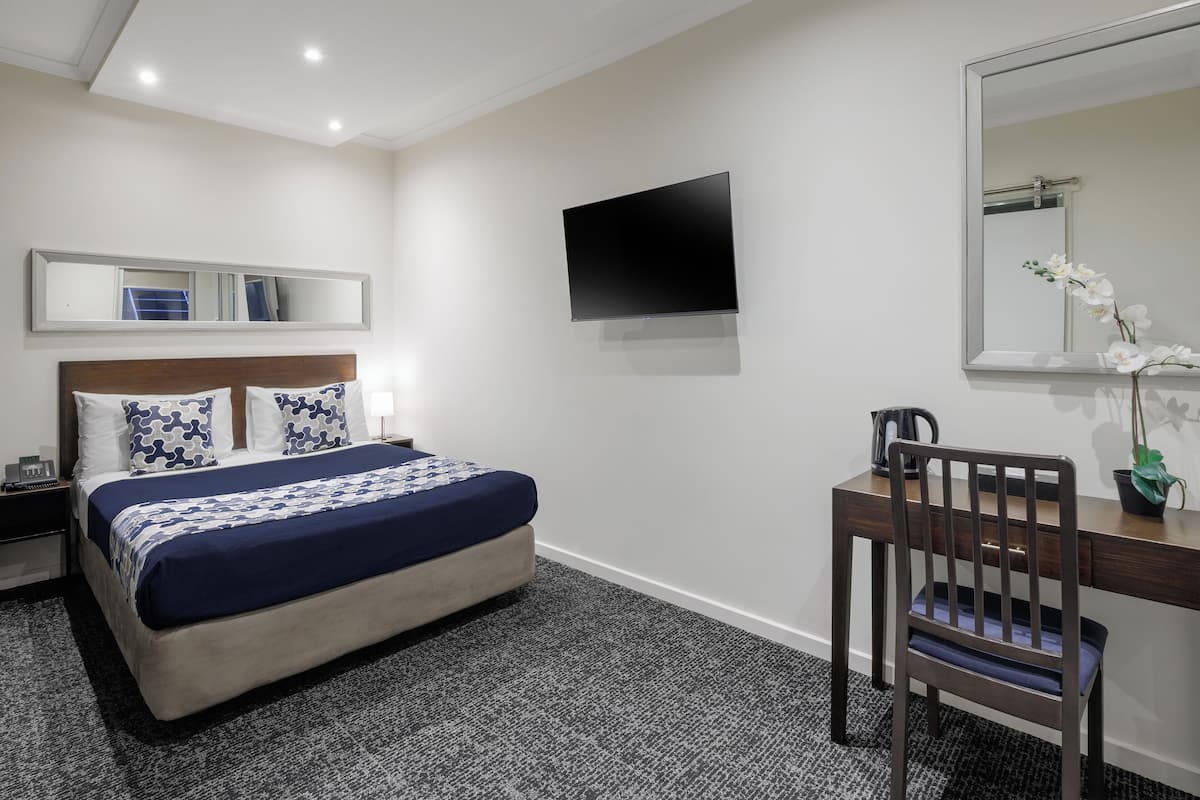 Habitación de hotel con cama, escritorio, silla, televisor de pantalla plana y espejo.