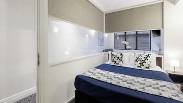 Une chambre d’hôtel avec un grand lit, une table de chevet avec une lampe, une fenêtre donnant sur un beau paysage et une étagère fixée au mur.