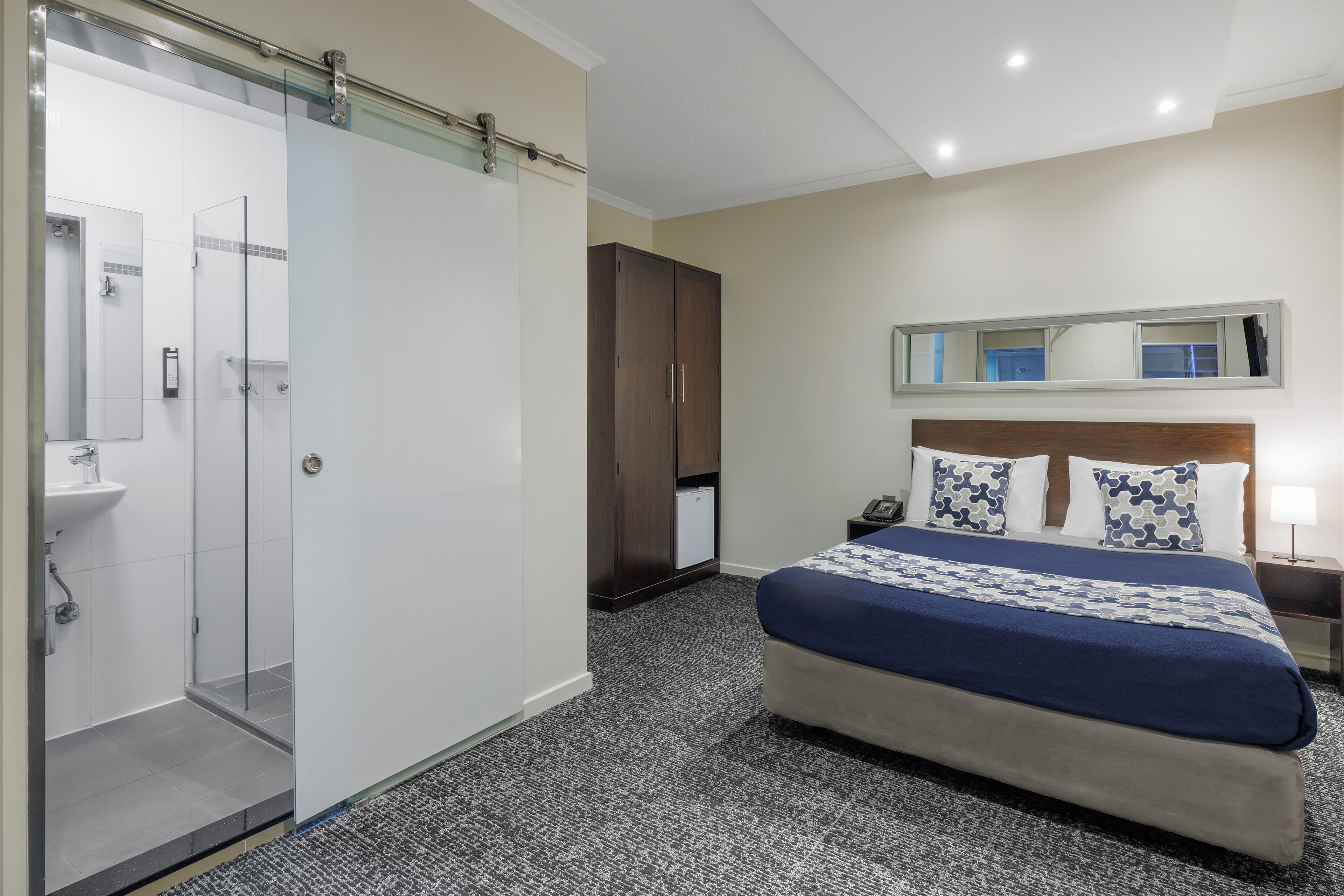 A hotel room with a bed, a wardrobe, a mirror, and a shower area.