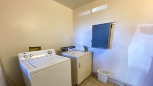 A laundry room with a front-loading washer and dryer, a sink, and a small trash bin.