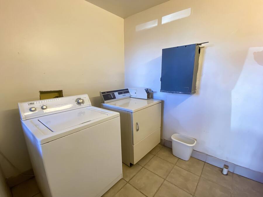 A laundry room with a front-loading washer and dryer, a sink, and a small trash bin.