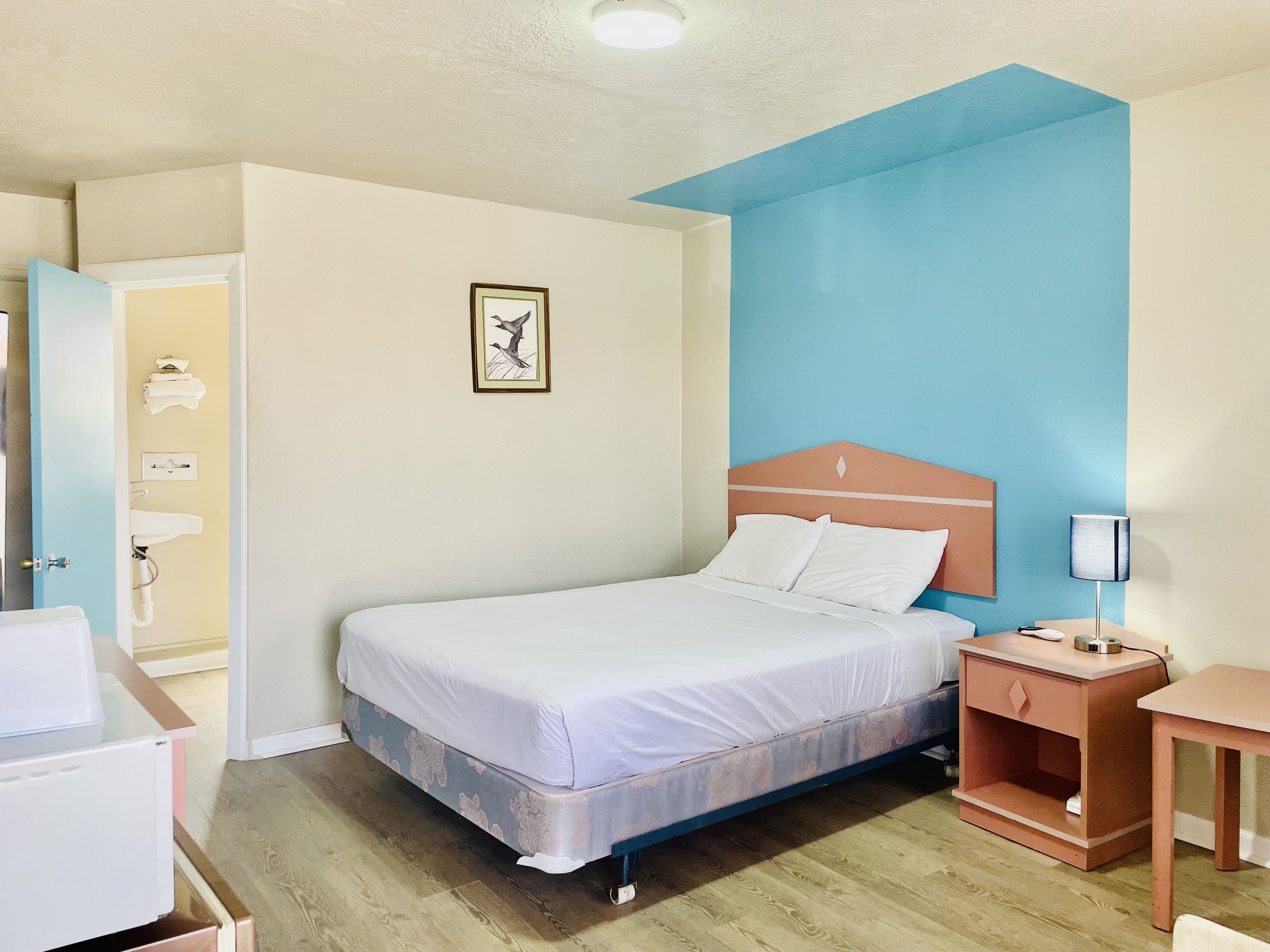 A hotel room with a bed, bedside table, nightstand, and a wall-mounted picture.