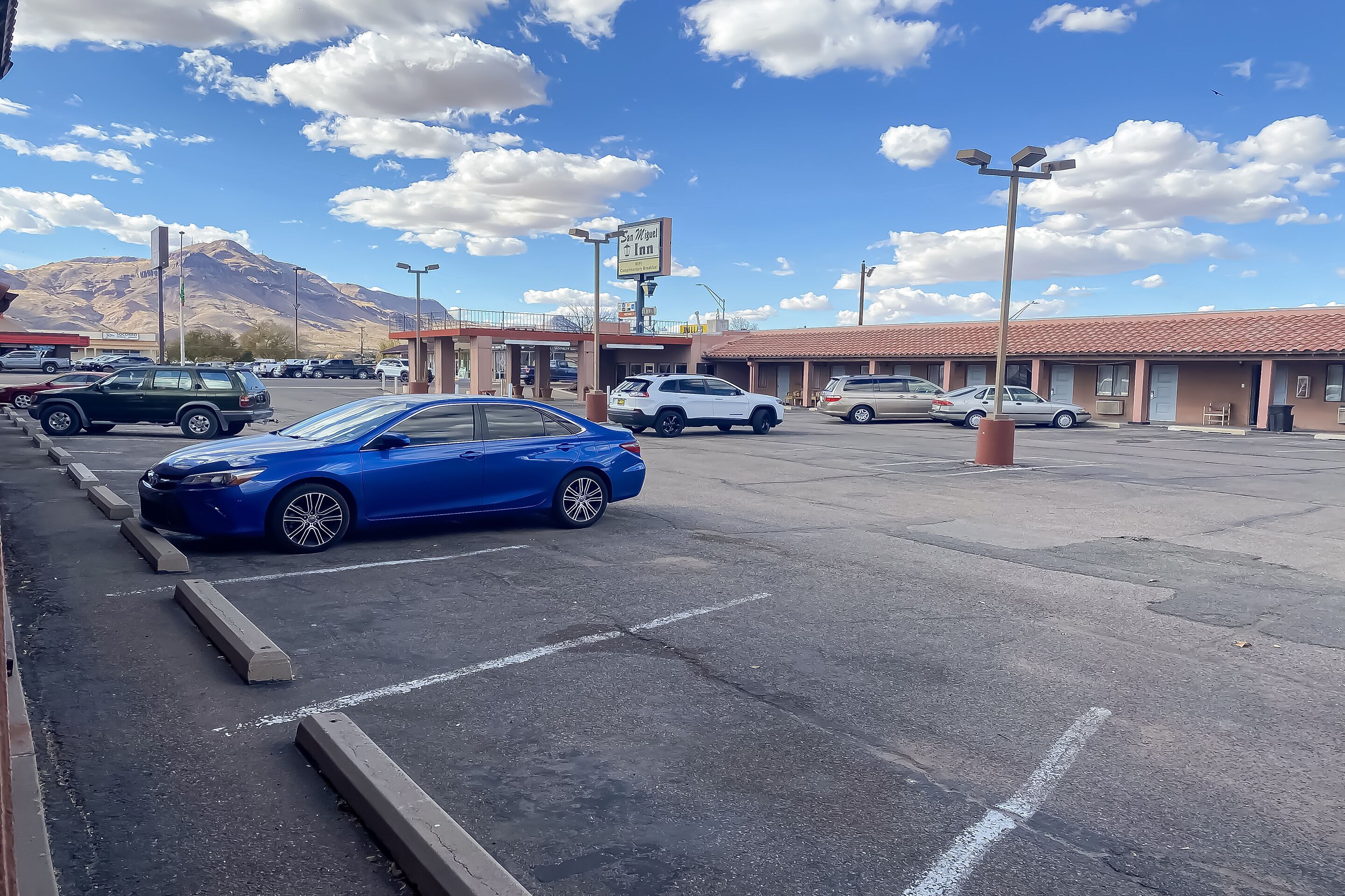 A parking lot with several cars, a motel with a red roof, and a mountain in the background.