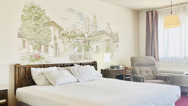 A hotel room with a large bed, a chair, a desk, and a wall mural.