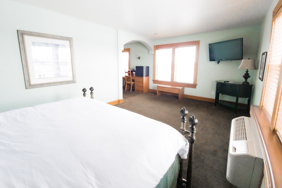 A hotel room with a large bed, a desk, a chair, a television, and a window.