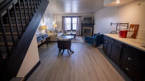Une cuisine moderne avec des meubles de couleur sombre, un coin repas avec une table ronde et des chaises, un canapé et un escalier.