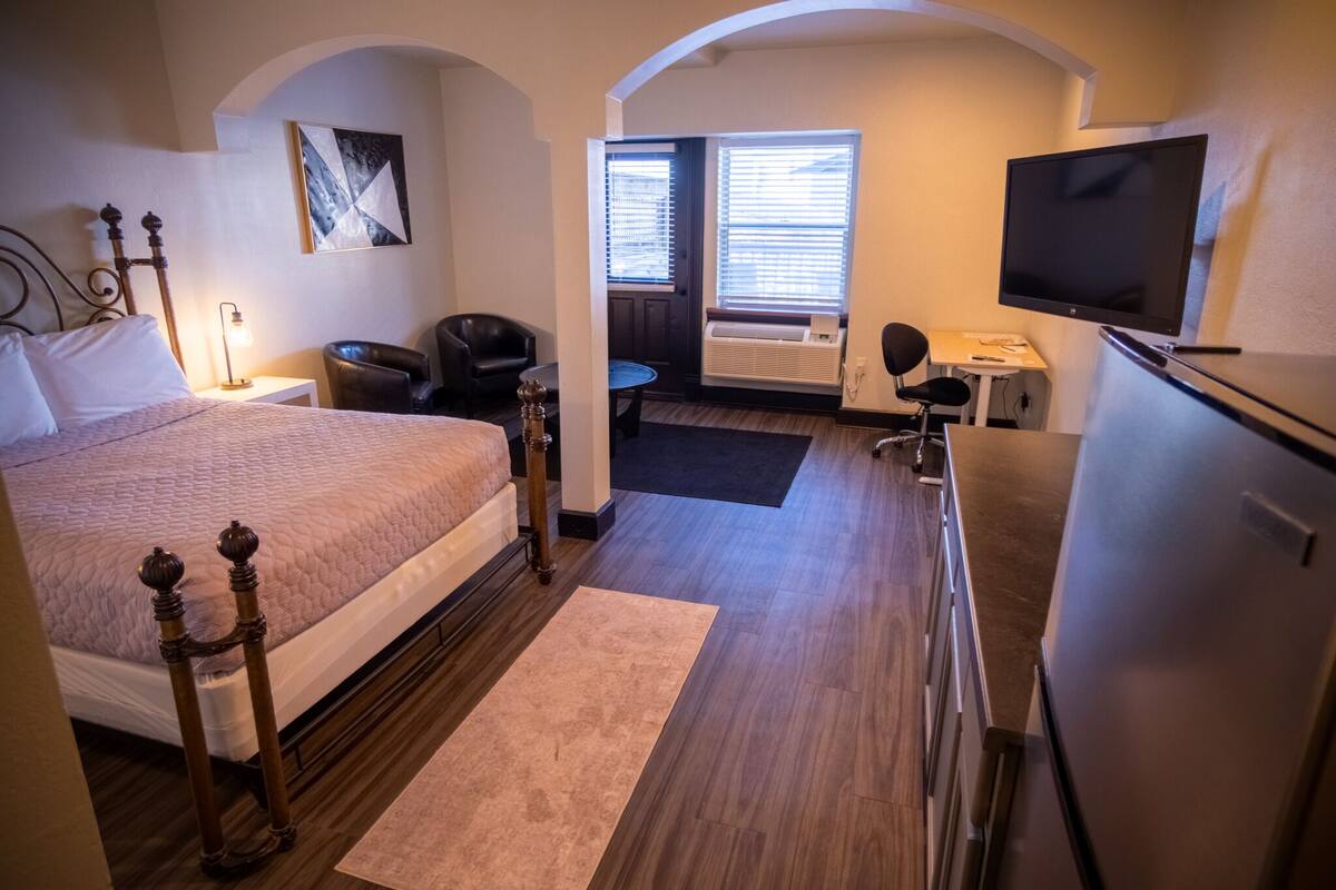 A hotel room with a bed, a desk, a chair, a television, and a window with blinds.