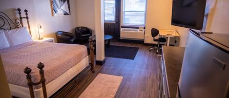 A hotel room with a bed, a desk, a chair, a television, and a window with blinds.