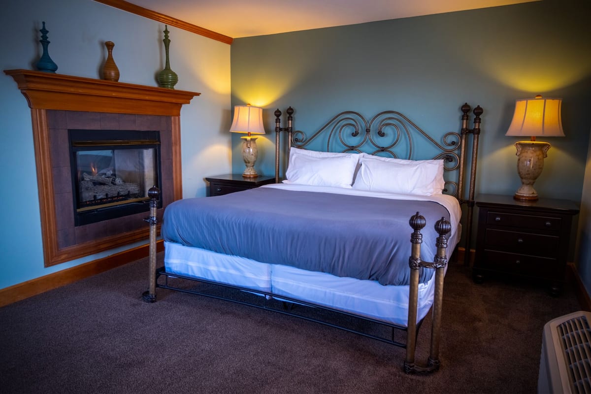 A neatly arranged bedroom with a bed, nightstands, a fireplace, and lamps.