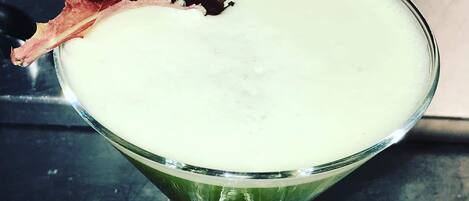 A martini glass with a green liquid, garnished with a leaf and a slice of red fruit.