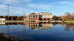 Un bâtiment situé au bord de l’eau, dont le reflet se mire dans l’eau, avec un quai et un ciel dégagé.