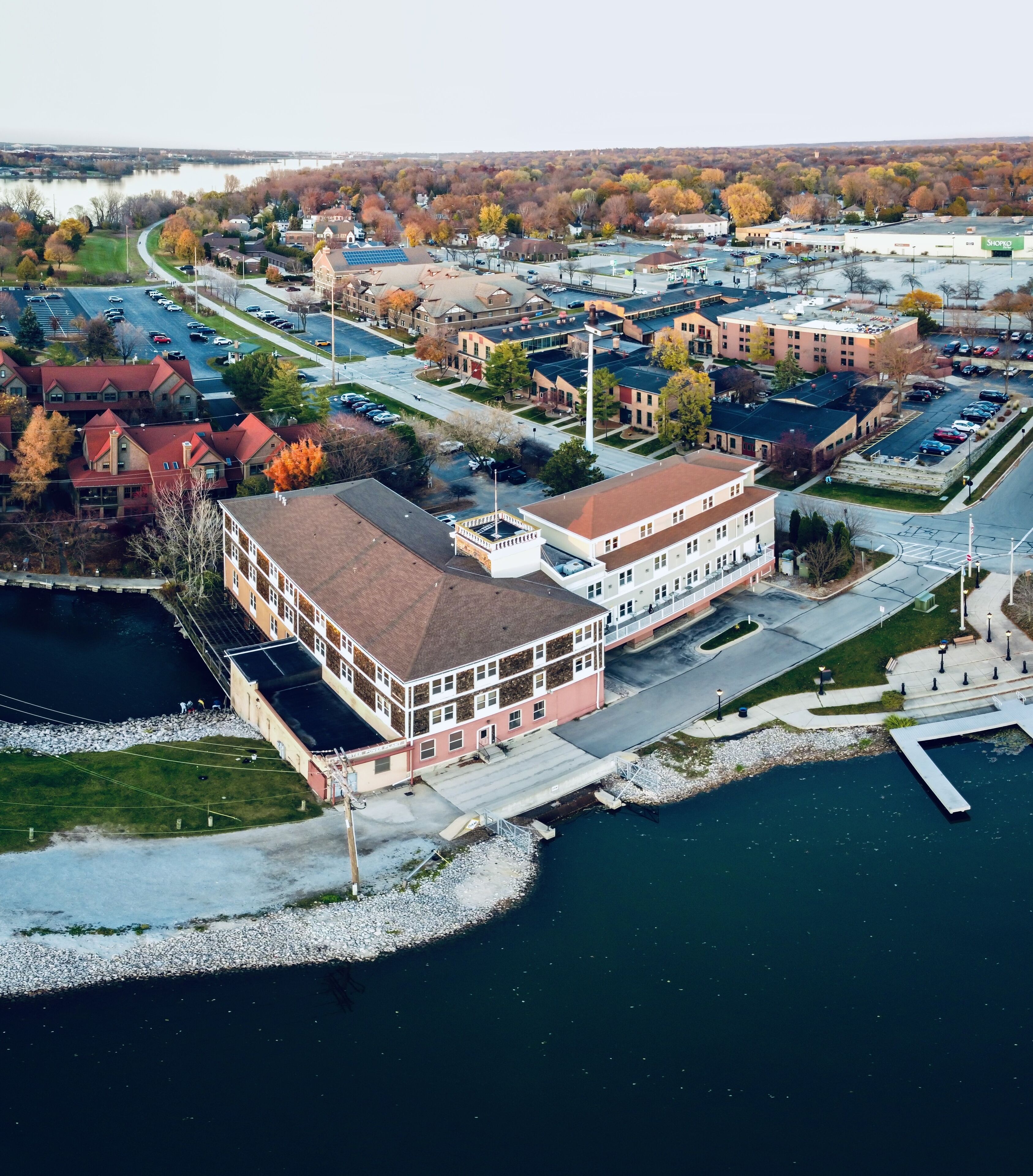 An aerial view of a waterfront property with a large building featuring multiple floors, a dock, and a parking area.