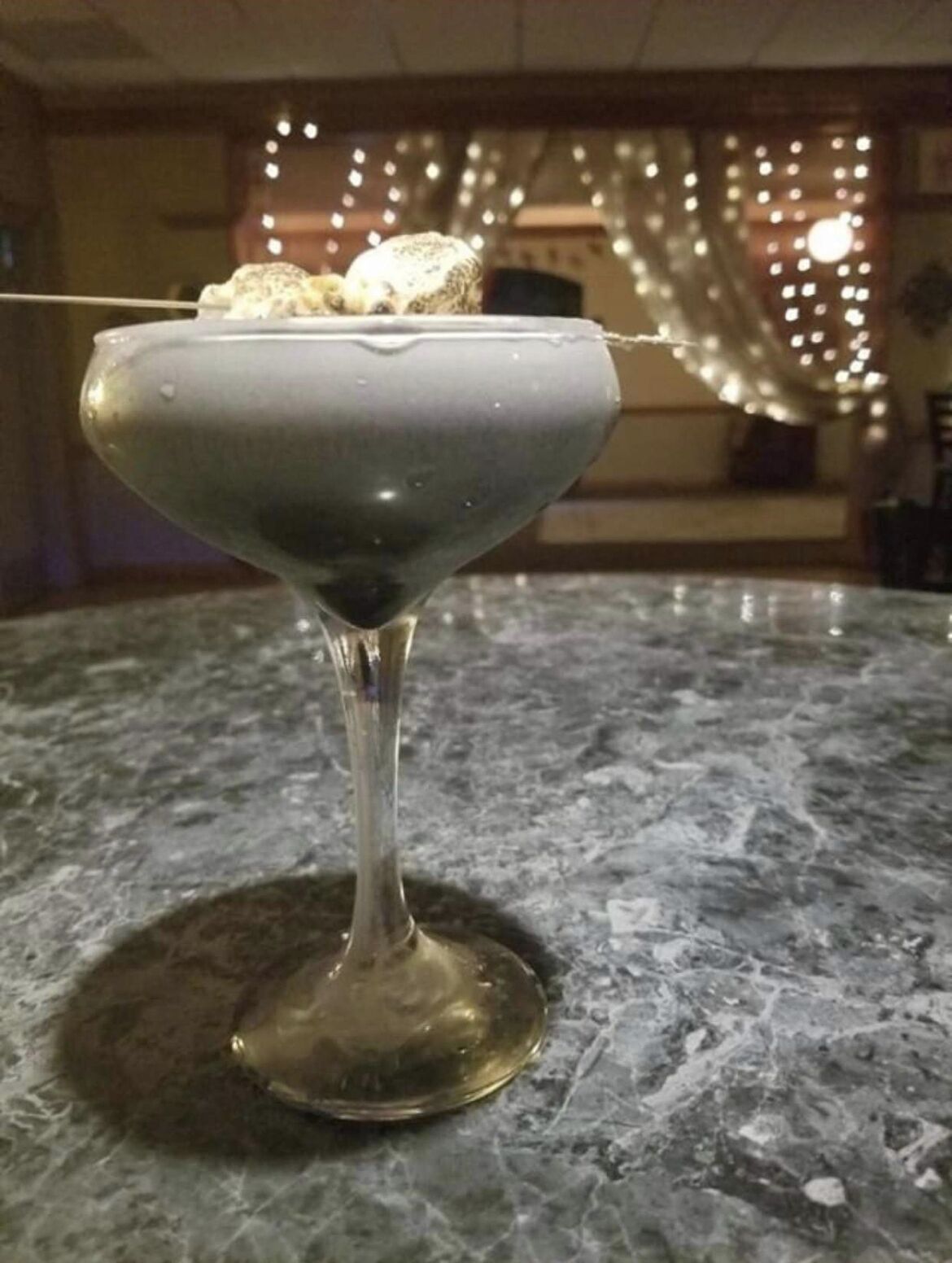 Una copa de martini con un líquido transparente sobre una encimera de mármol.