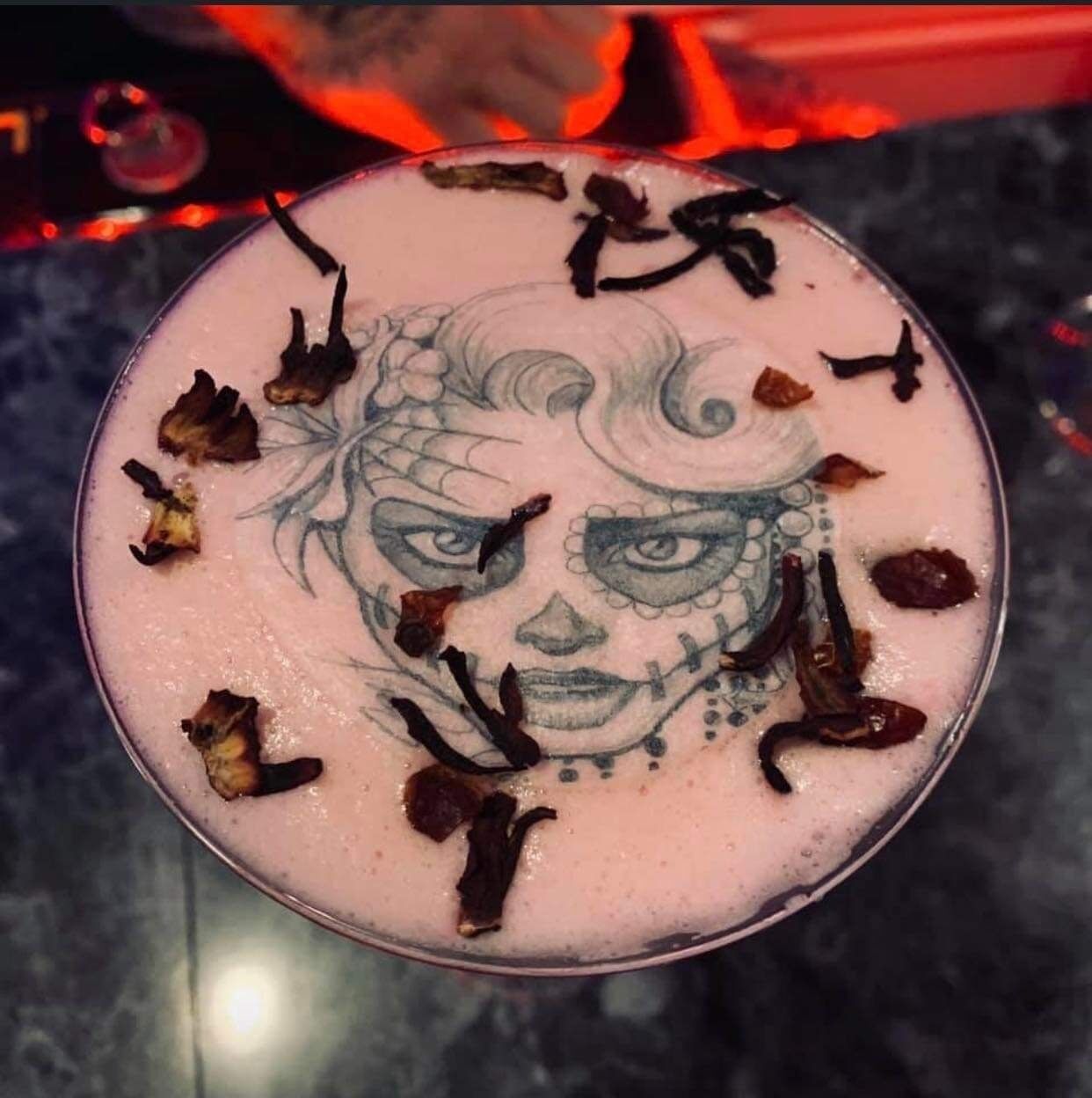 Una copa redonda de vidrio con una bebida rosada, decorada con flores secas y un diseño facial.