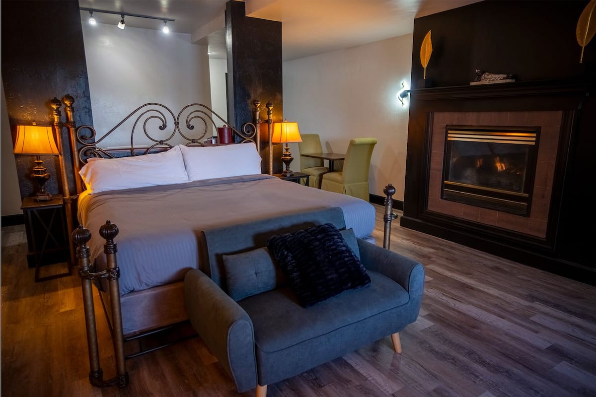 A neatly arranged bedroom with a bed, a sofa, a fireplace, and two lamps.