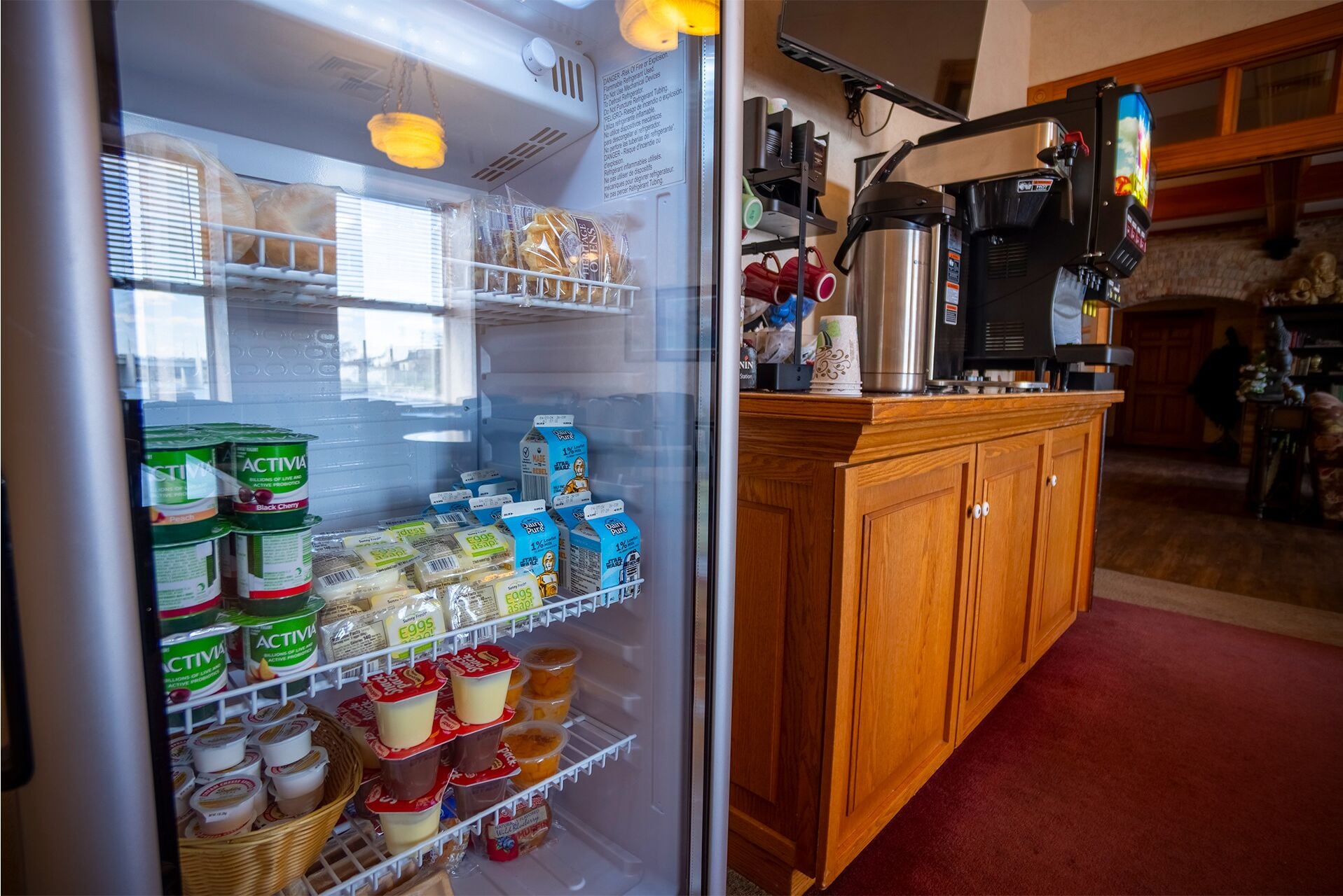 Una cocina con un refrigerador lleno de productos lácteos, una máquina de café y un armario de madera.