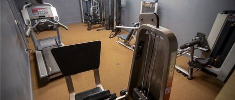 Une salle de sport équipée de divers appareils d’exercice, notamment des tapis de course, des appareils de musculation et un banc de développé couché.