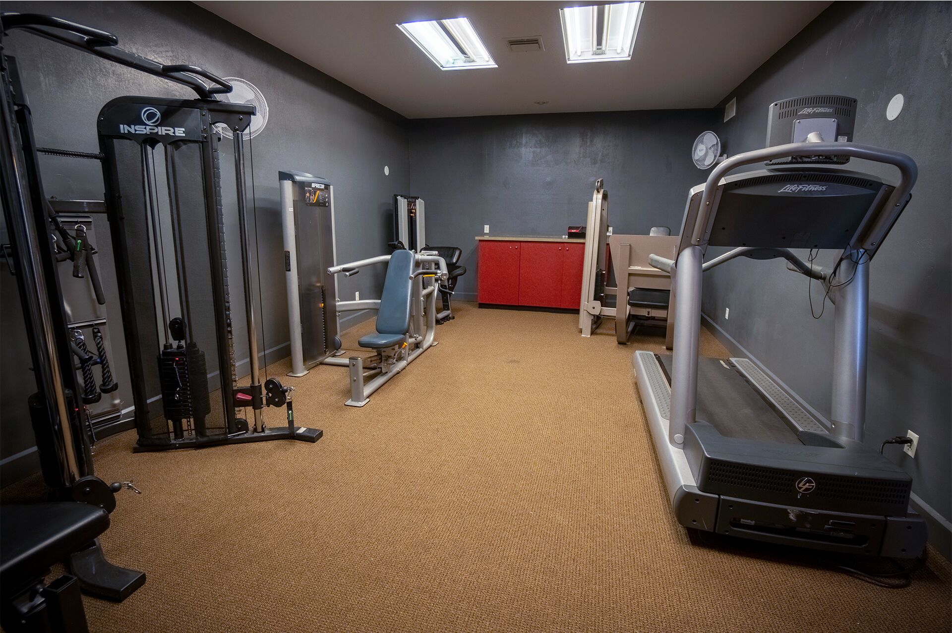 A gym with various exercise machines, a red cabinet, and a treadmill.