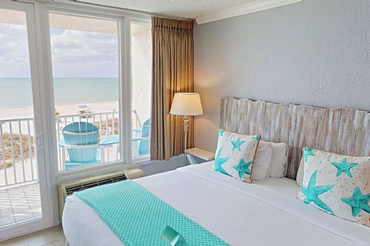 A hotel room with a large bed, a view of the beach, and a balcony with chairs.