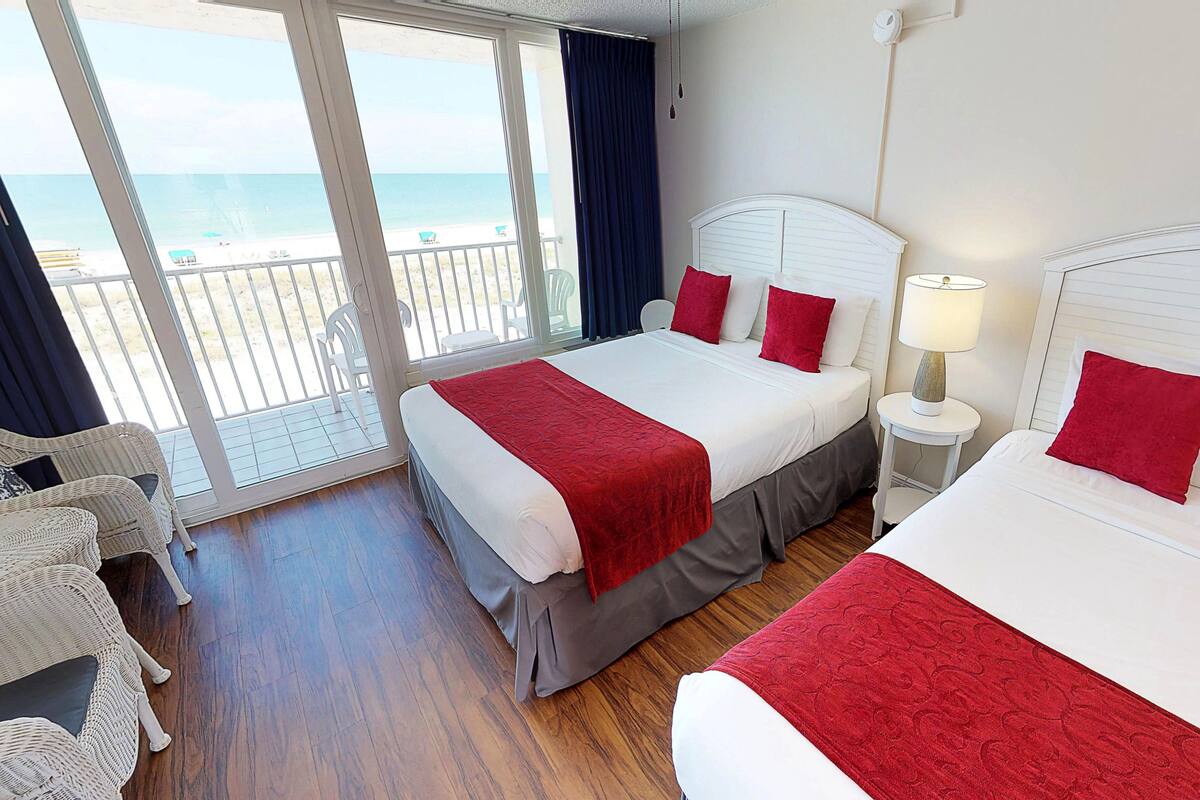 A hotel room with two beds, a balcony with a view of the beach, and a white headboard.