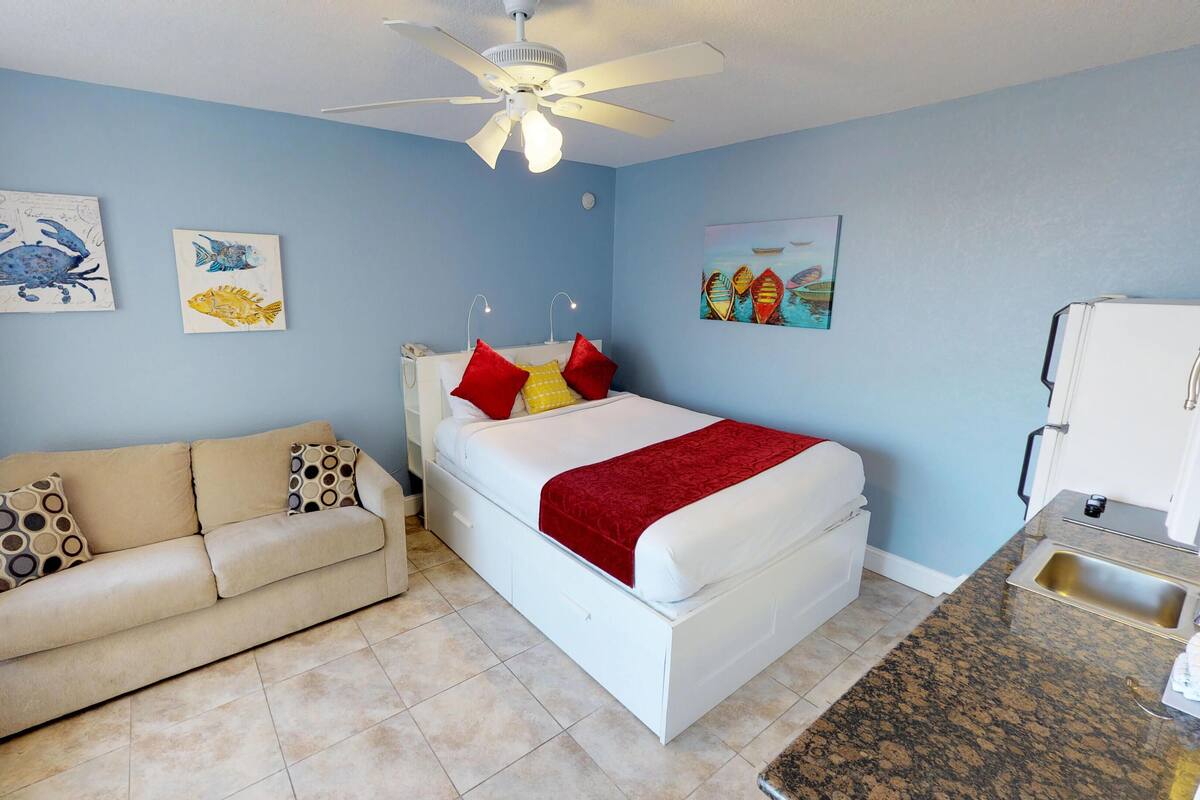 A bedroom with a bed, a couch, a ceiling fan, and artwork on the walls.