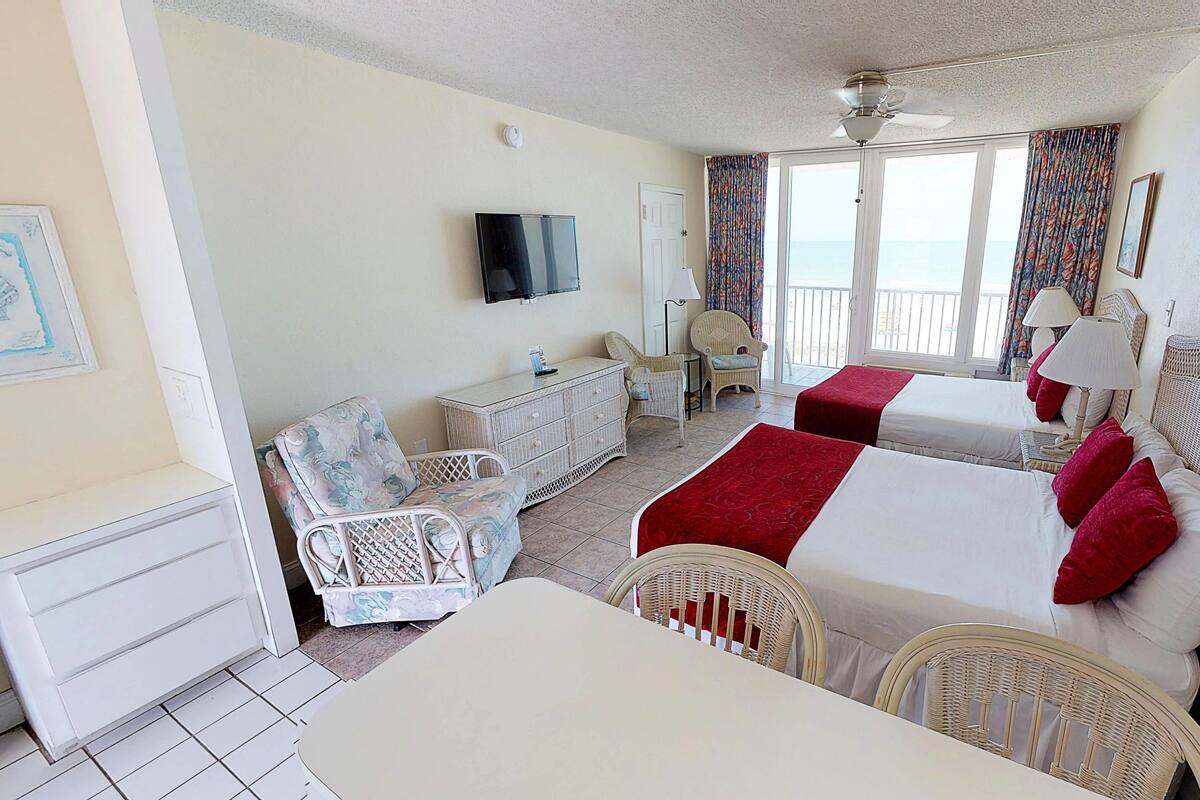 A hotel room with two beds, a desk, a chair, a television, and a balcony with a view.