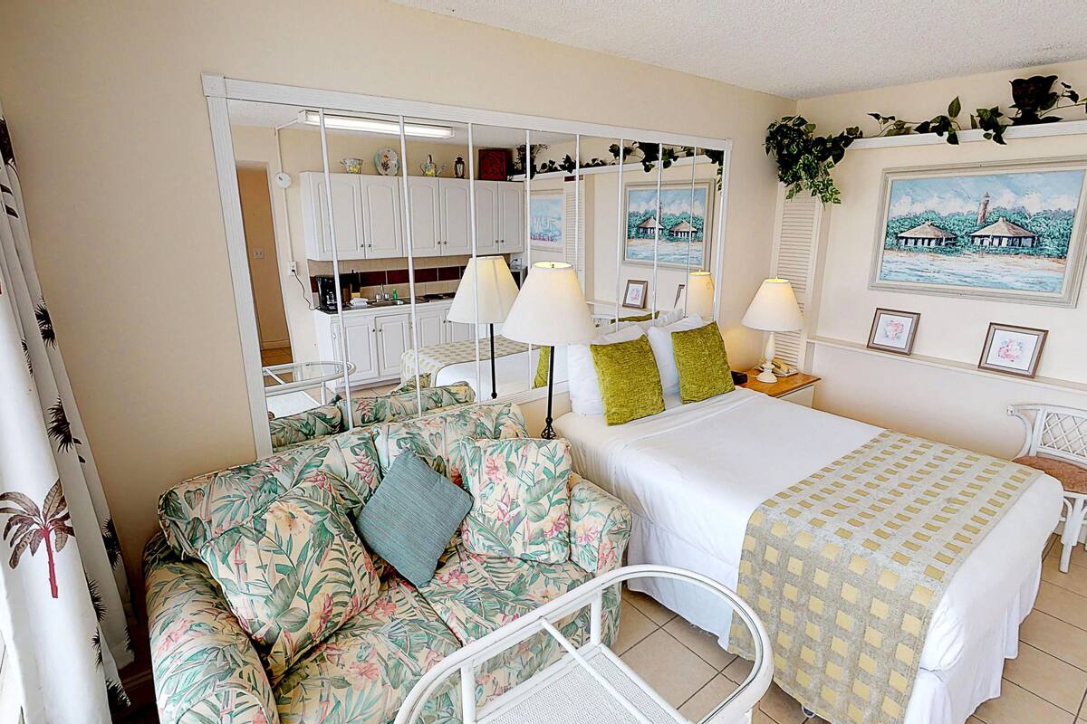 A room with a bed, a sofa, a chair, a small table, and a cabinet.