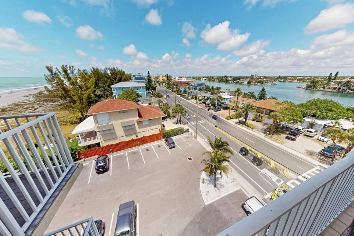 A view from a balcony overlooking a beach, a parking lot, and a body of water.