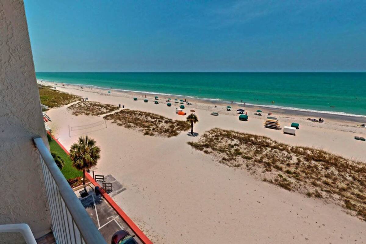 A beach view from a balcony with a clear sky, sandy beach, and umbrellas.