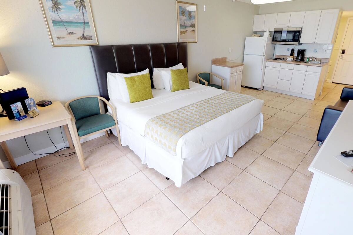 A hotel room with a bed, a desk, a chair, a kitchenette, and a bathroom.
