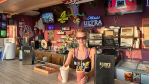 Un bar con un letrero de neón, un televisor y una variedad de botellas.