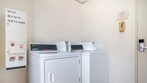 Une buanderie équipée de deux machines à laver et deux sèche-linge à chargement frontal, d’un sèche-linge à pièces et d’un panneau indiquant les produits de lessive disponibles.