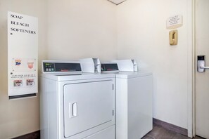 Une buanderie équipée de deux machines à laver et deux sèche-linge à chargement frontal, d’un sèche-linge à pièces et d’un panneau indiquant les produits de lessive disponibles.