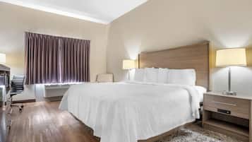 A hotel room with a large bed, two bedside lamps, a desk with a chair, a window with curtains, and a wall-mounted air conditioner.