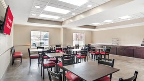 A spacious dining area with multiple tables and chairs, a kitchen area, and a view of the street through large windows. - Red Roof Inn PLUS+ & Suites Vicksburg (Vicksburg)