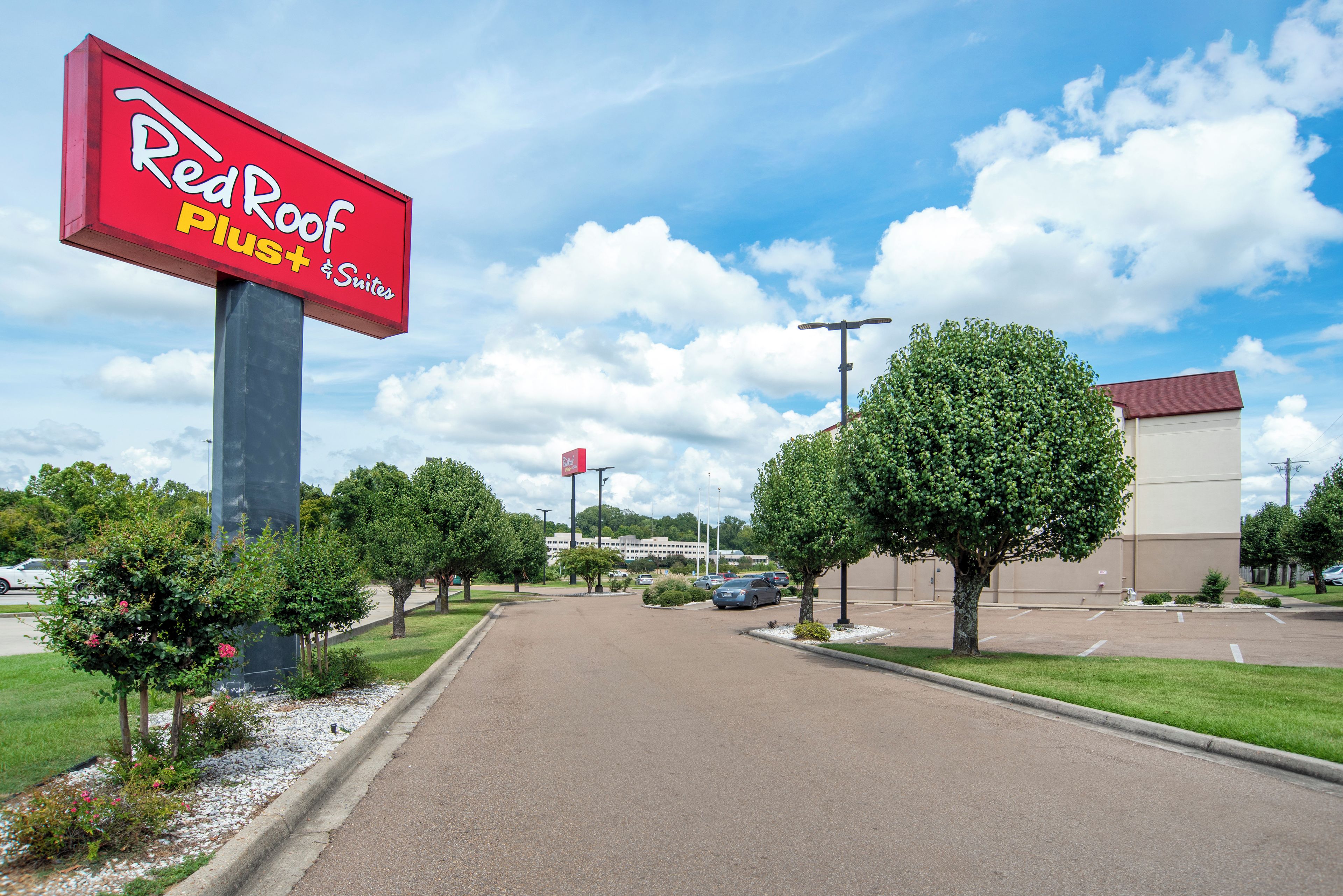 Ein Schild von Red Roof Plus & Suites, ein Parkplatz und ein Gebäude im Hintergrund.