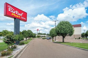 Señal de Red Roof Plus & Suites, un estacionamiento y un edificio al fondo.