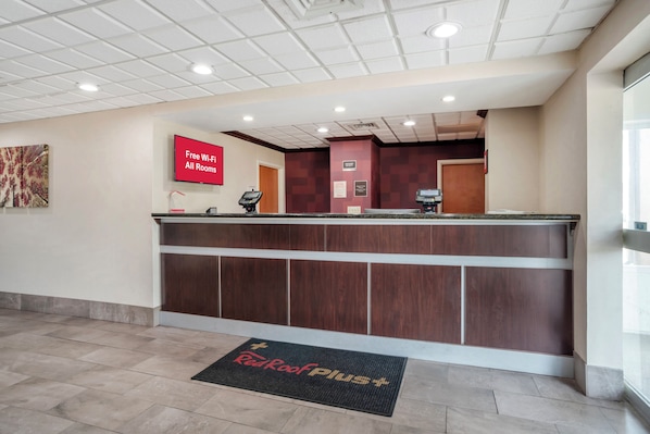 A hotel reception area with a flat-screen TV displaying 'Free Wi-Fi All Rooms' and a check-in counter.