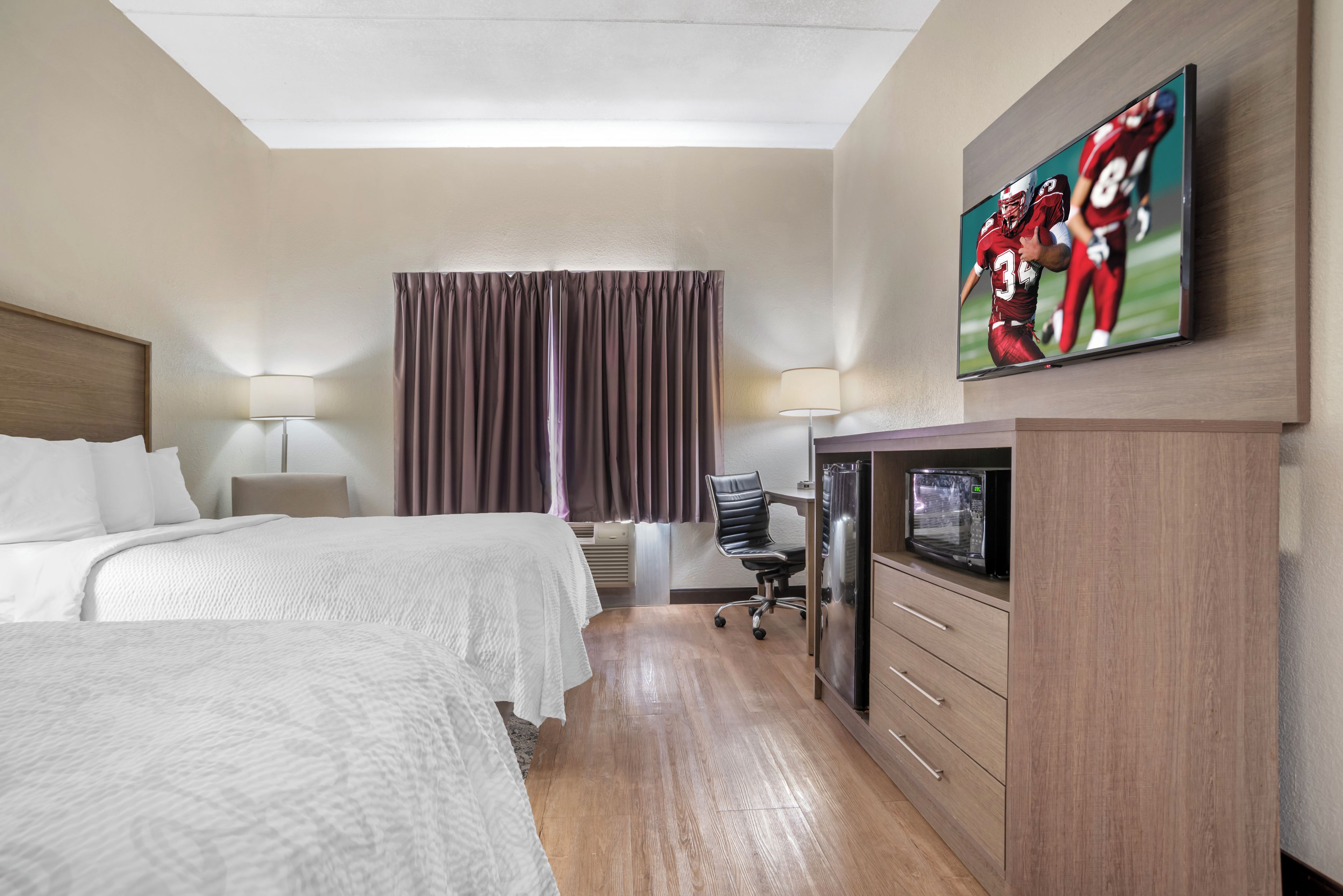 A hotel room with two beds, a desk, a chair, a television, and a window with curtains.