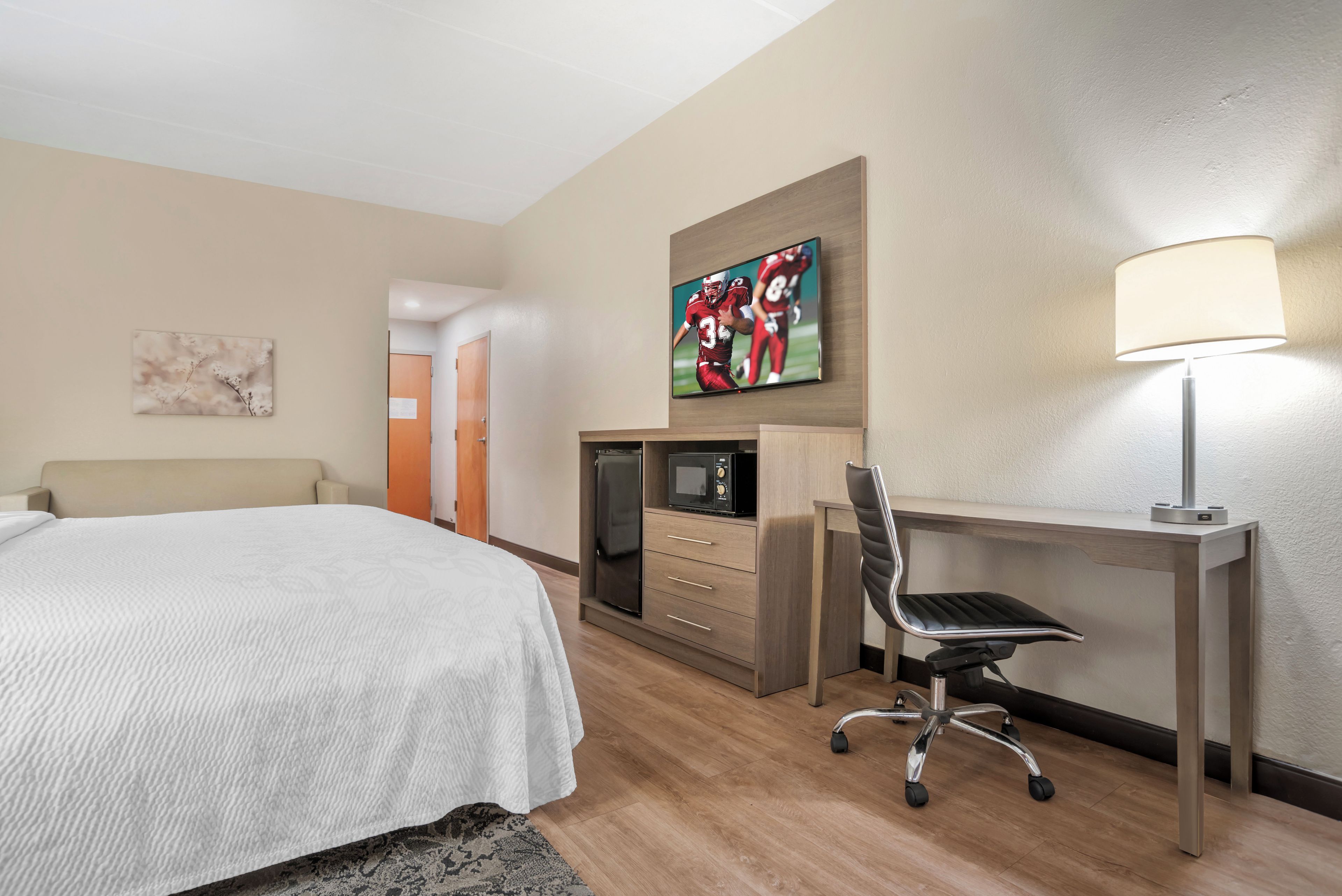 A hotel room with a bed, a desk with a chair, a TV, a microwave, and a lamp.