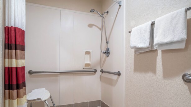 A bathroom with a shower, grab bars, a toilet with a raised seat, and a towel rack. - Red Roof Inn PLUS+ & Suites Vicksburg (Vicksburg)
