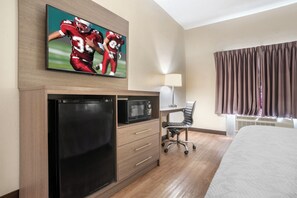 A hotel room with a bed, a desk with a chair, a television mounted on the wall, and a microwave.