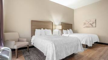 A hotel room with two beds, a chair, a lamp, and a painting on the wall.