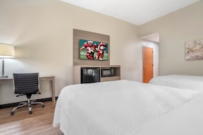 A hotel room with a bed, a desk with a lamp, a microwave, and artwork on the wall. - Red Roof Inn PLUS+ & Suites Vicksburg (Vicksburg)
